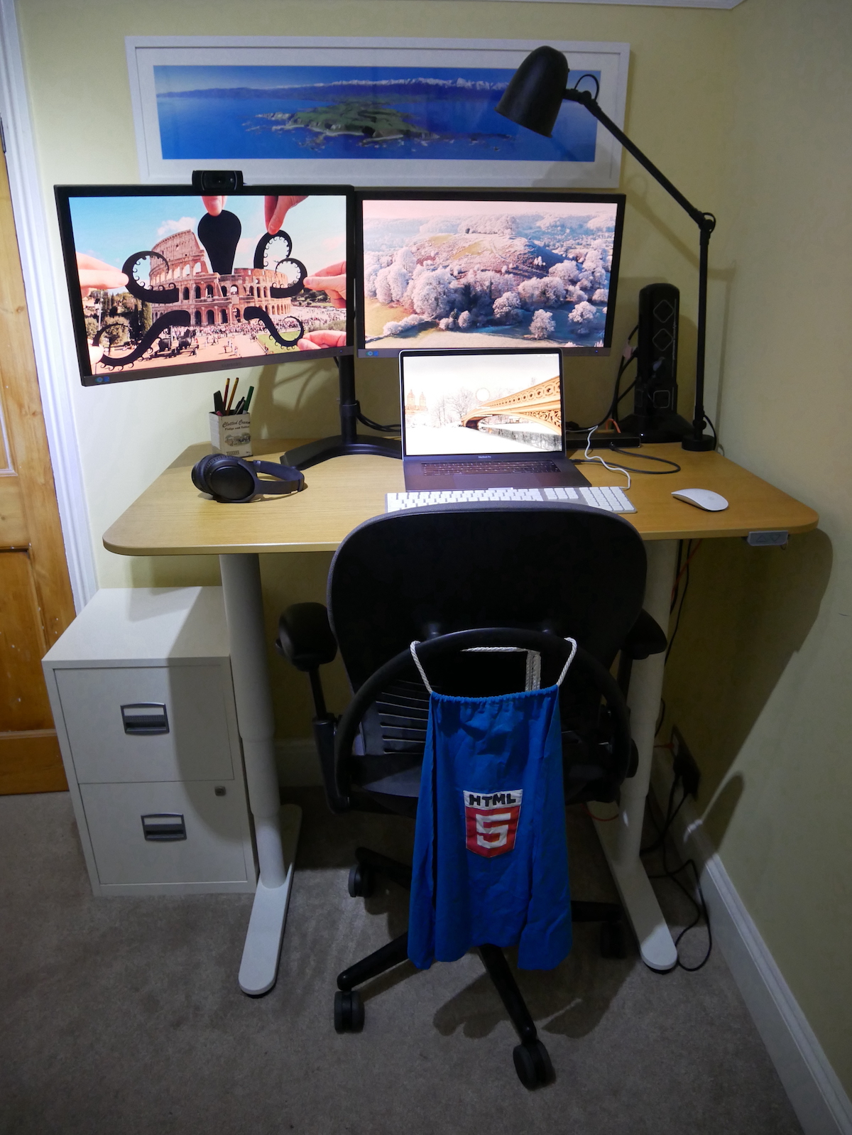A standing desk adorned with a 2018 Macbook Pro and two external monitors, flanked by a Steelcase Leap chair